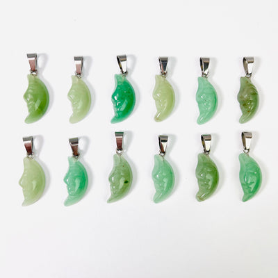 Twelve Green Aventurine Crescent Moon Gemstones Pendants lined up in two rows on a white surface.