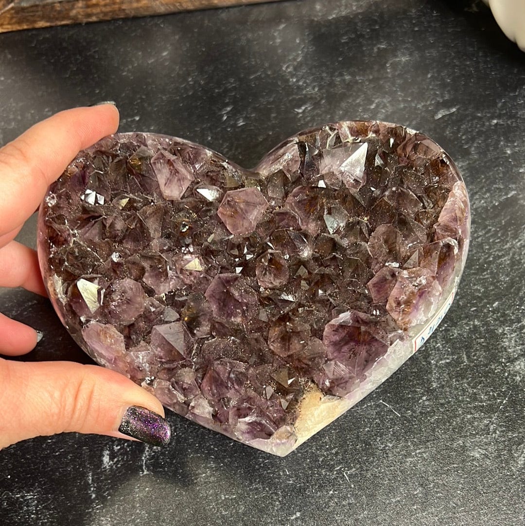 Amethyst cluster heart held on a black background.