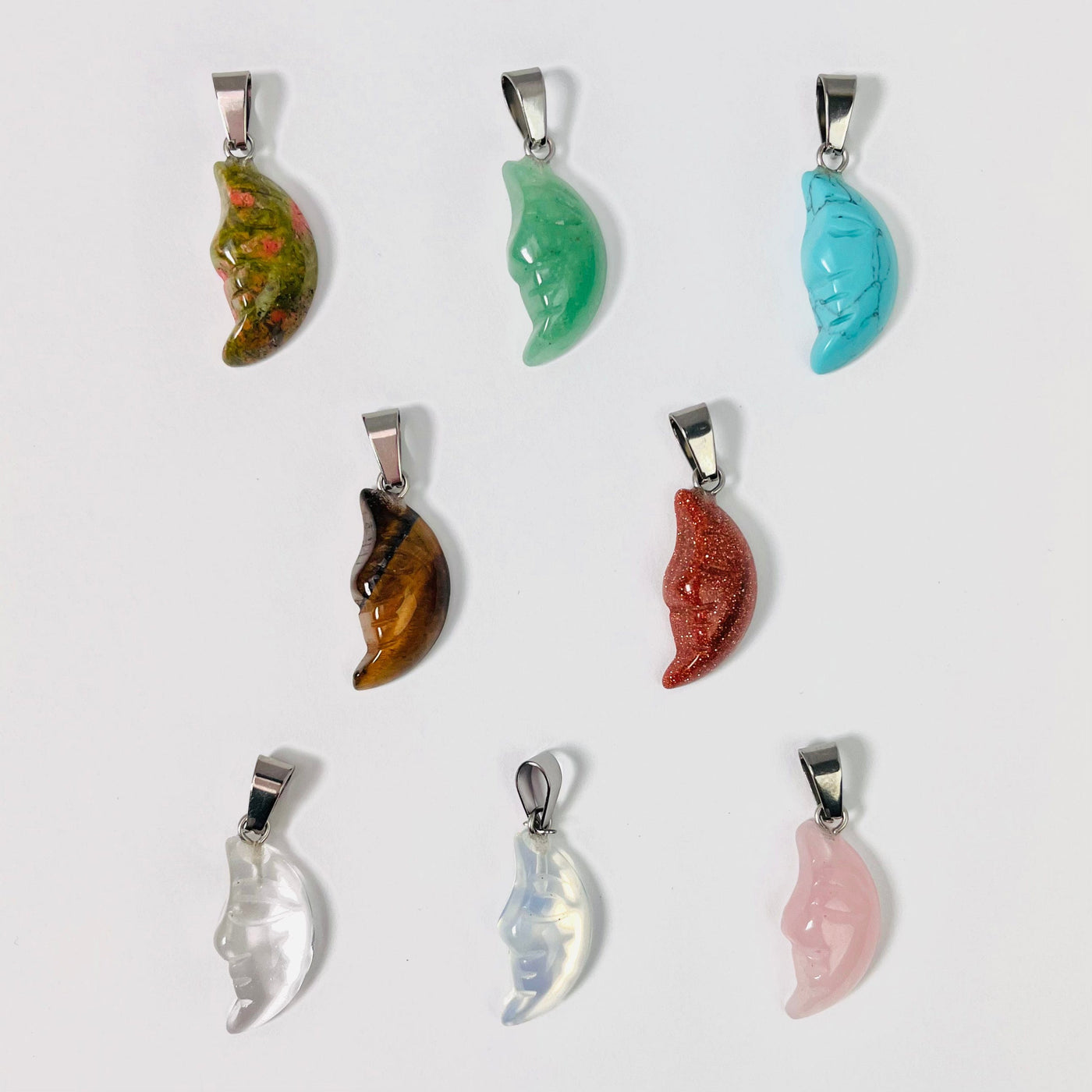 Eight Crescent Moon Gemstone Pendants set up in 3 lines; one of each stone displayed on a white surface.