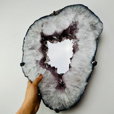 Frontal view of Light Color Amethyst Point Mirror, mounted on wall. Hand placed under for size reference
