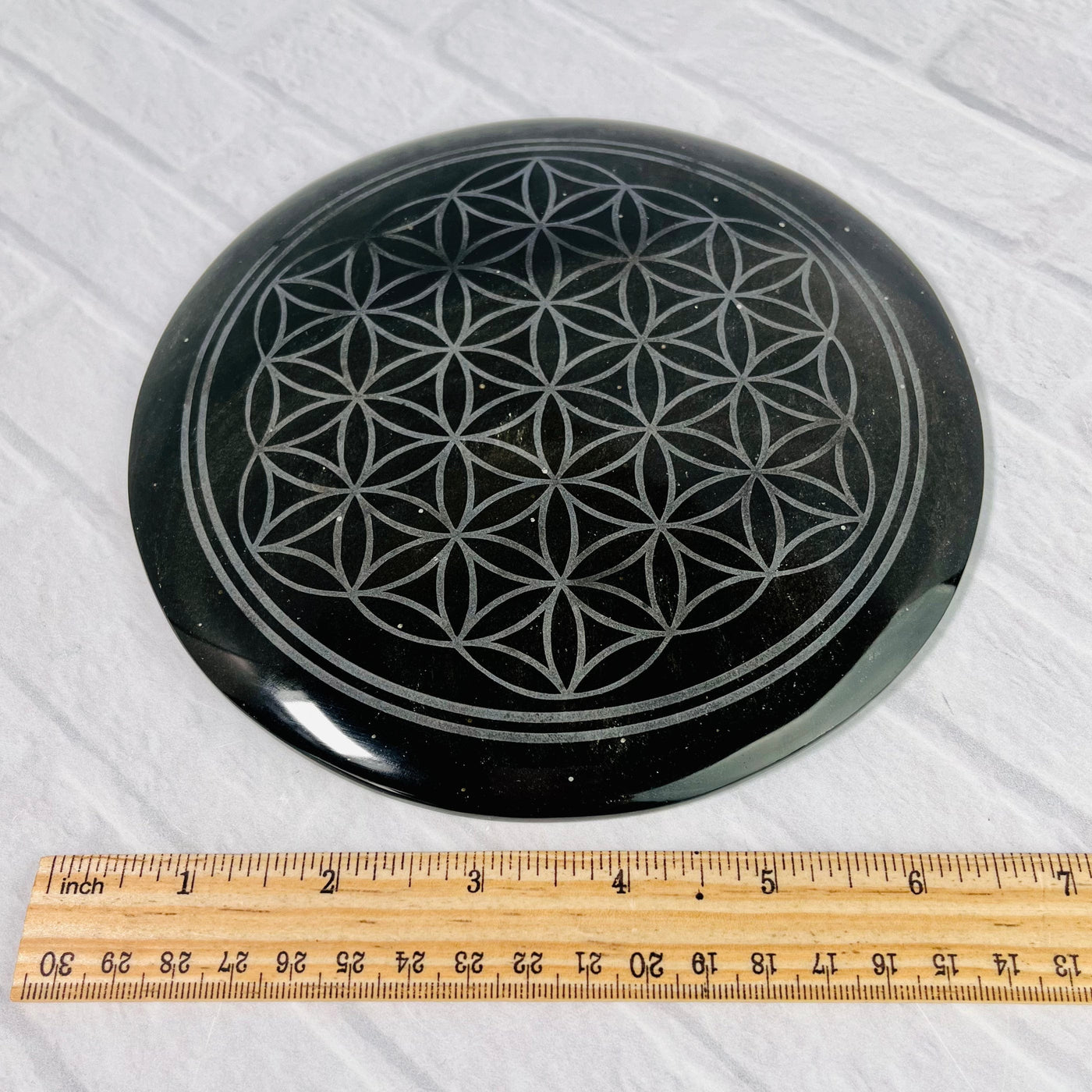 Gold Sheen Obsidian Flower of Life Plate displayed on a white surface next to ruler for size reference.
