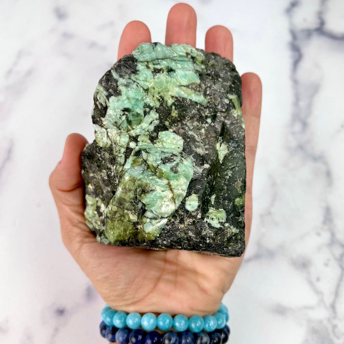 Rough Emerald Matrix stone "A" in the palm of woman's hand for size reference.