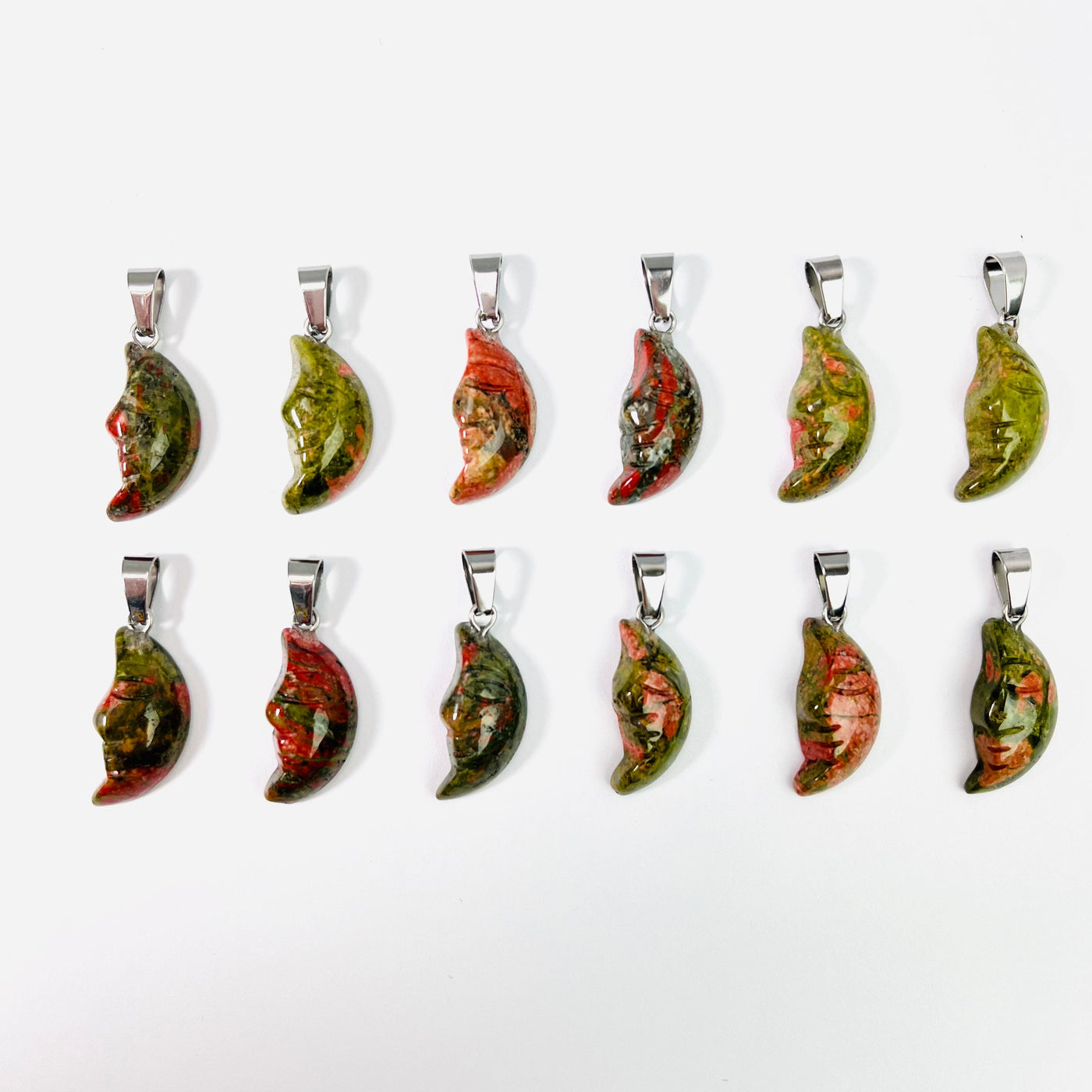 Twelve Unakite Crescent Moon Gemstones Pendants lined up in two rows on a white surface.