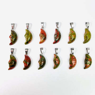 Twelve Unakite Crescent Moon Gemstones Pendants lined up in two rows on a white surface.