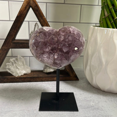 Amethyst cluster heart on a black metal stand.