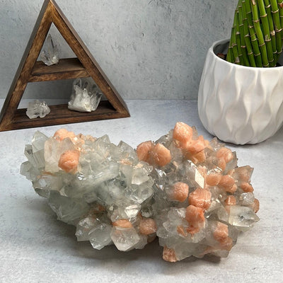 Large zeolite cluster with apophyllite and peach stillbite crystals on a gray background with some props.