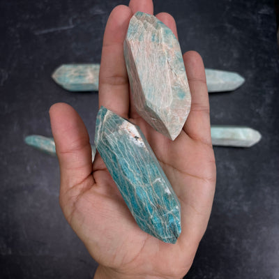 Two Amazonite Polished Double Terminated Points, in the weight range of 50g-100g, laying in palm of woman's hand.