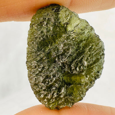 6.4 gram (option J) Moldavite piece held up between woman's fingers.