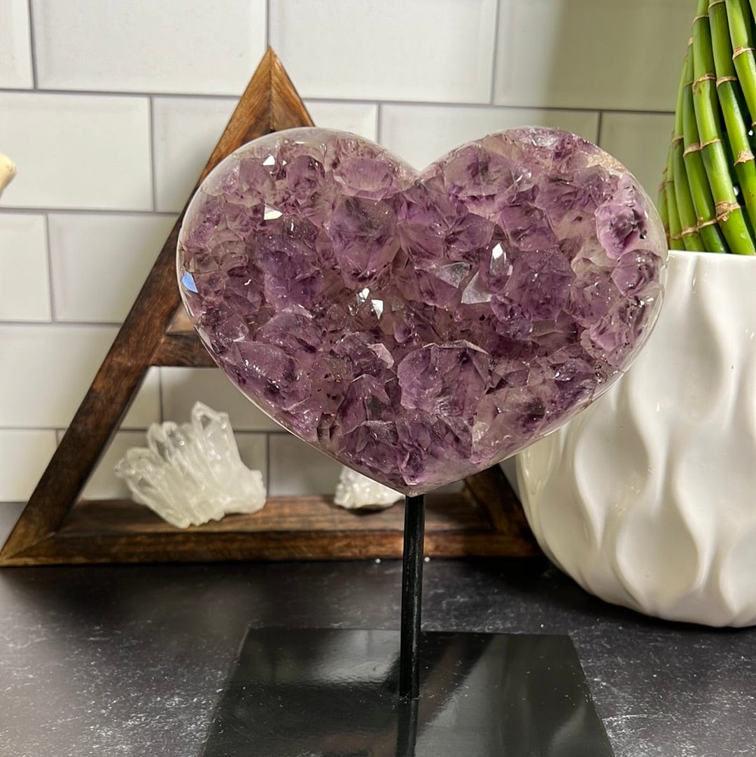 Amethyst cluster heart on a black metal stand pictured on a black background.