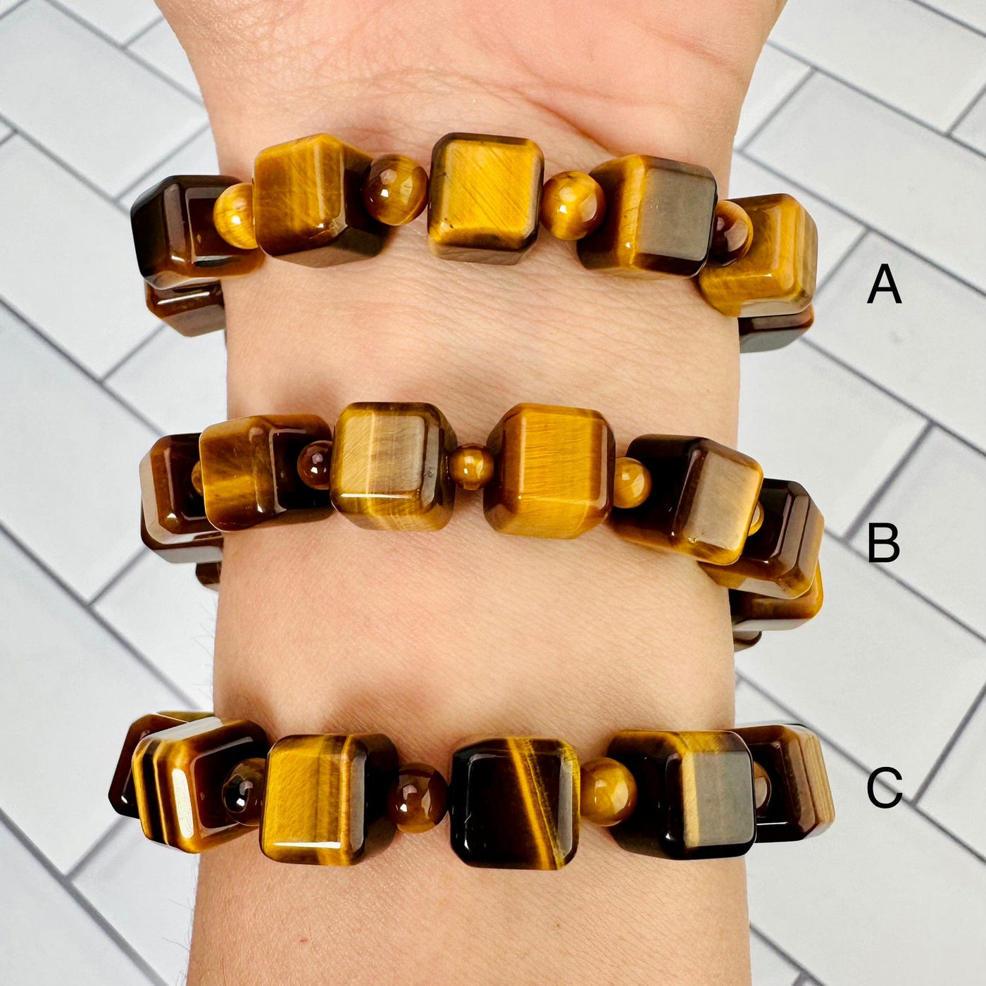 3 different sizes of tigers eye bracelets displayed on woman's wrist, with respective letter next to each one.