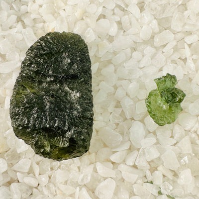 Largest and smallest Moldavite pieces next to each other on top of crystal quartz chips.