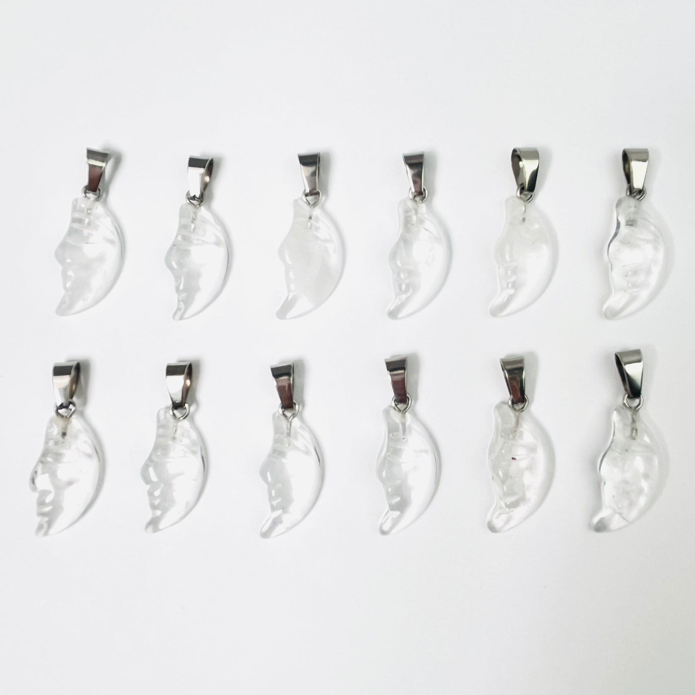 Twelve Crystal Quartz Crescent Moon Gemstones Pendants lined up in two rows on a white surface.