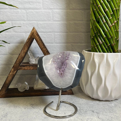 Agate polished stone with amethyst in the center on a silver metal base pictured on a gray background.