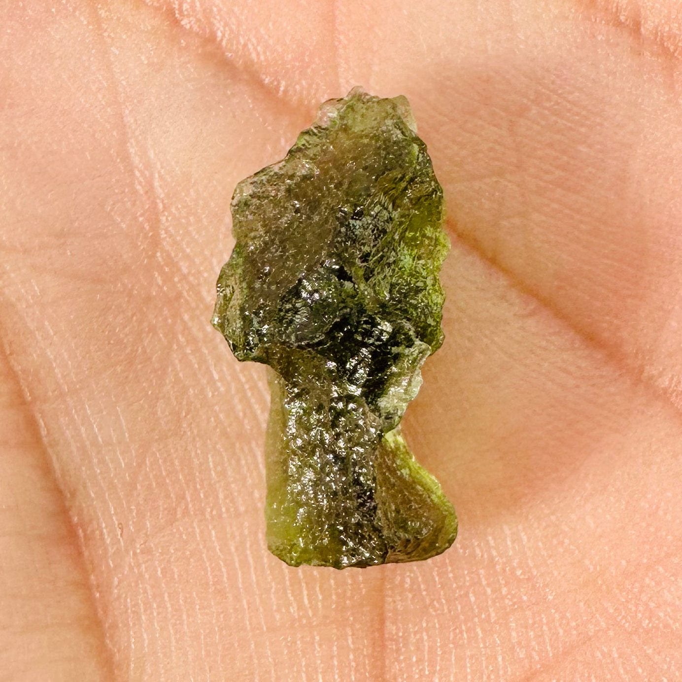 Up close view of 0.9 gram (option B) Moldavite piece displayed in palm of woman's hand. 