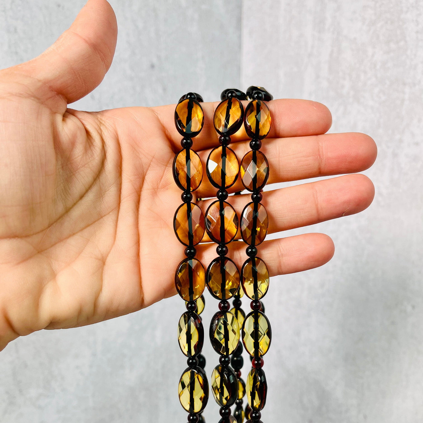Three Baltic Amber Beaded Necklaces hanging over a woman's hand.