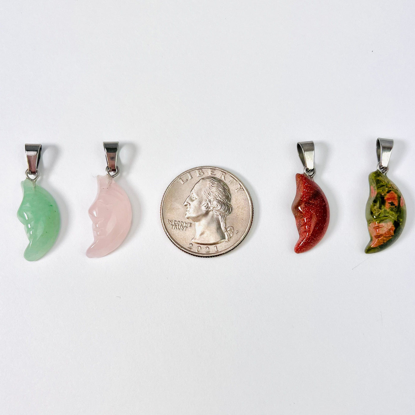 Four Crescent Moon Gemstone Pendants in a line with a quarter in the middle for size reference.
