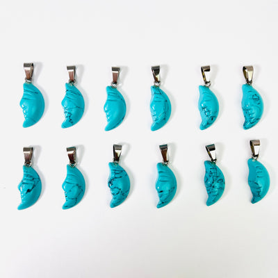 Twelve Howlite Crescent Moon Gemstones Pendants lined up in two rows on a white surface.