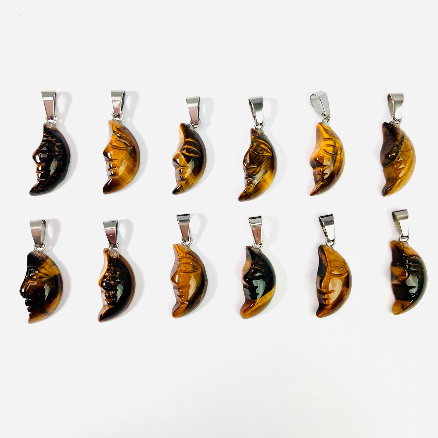 Twelve Tigers Eye Crescent Moon Gemstones Pendants lined up in two rows on a white surface.