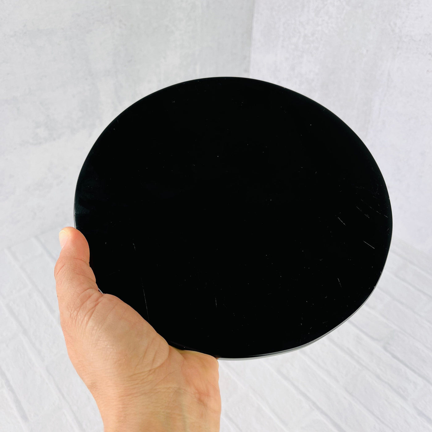 Back view of Black Obsidian Flower of Life Plate, held up by woman's hand.