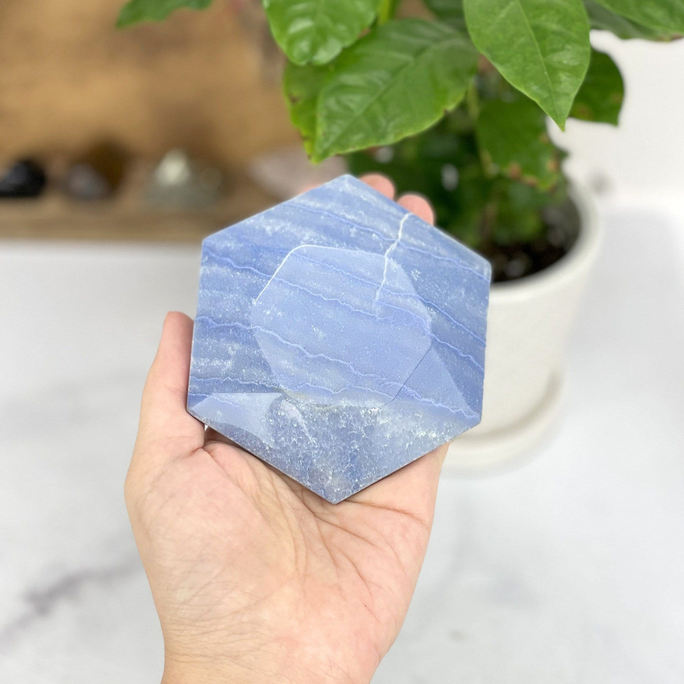 hand holding up Blue Quartz Hexagon with decorations in the background