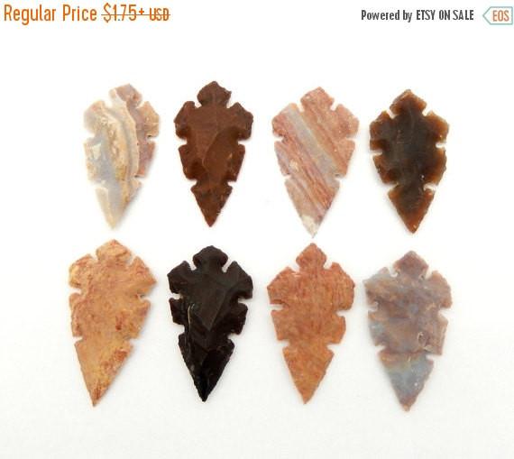 Multiple Jasper 2" Inch Arrow heads designed with indentation edge carvings displayed on white background showing various color shades of cream beige brown gray black and red hues