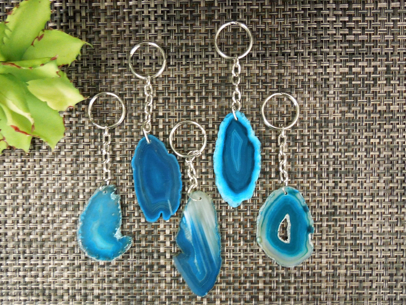 Multiple teal agate keychains on a dark colored background displaying color, size, pattern and shape variation.