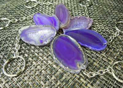 Multiple purple agate keychains on a dark colored background displaying color, size, pattern and shape variation.