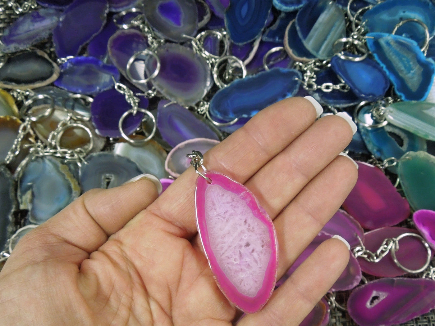 One pink agate keychain in a hand. Multiple agate keychains in the background.