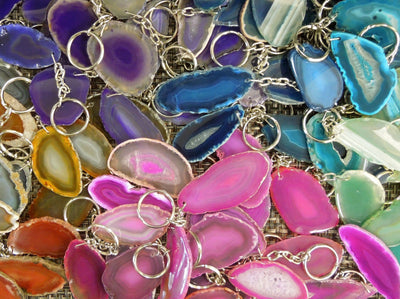 Multiple agate keychains on a dark colored background displaying color, shape and pattern variation.