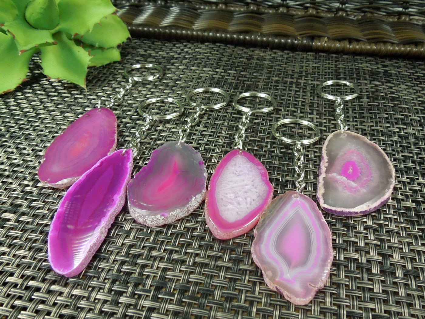 Multiple pink agate keychains on a dark colored background displaying color, size, pattern and shape variation.