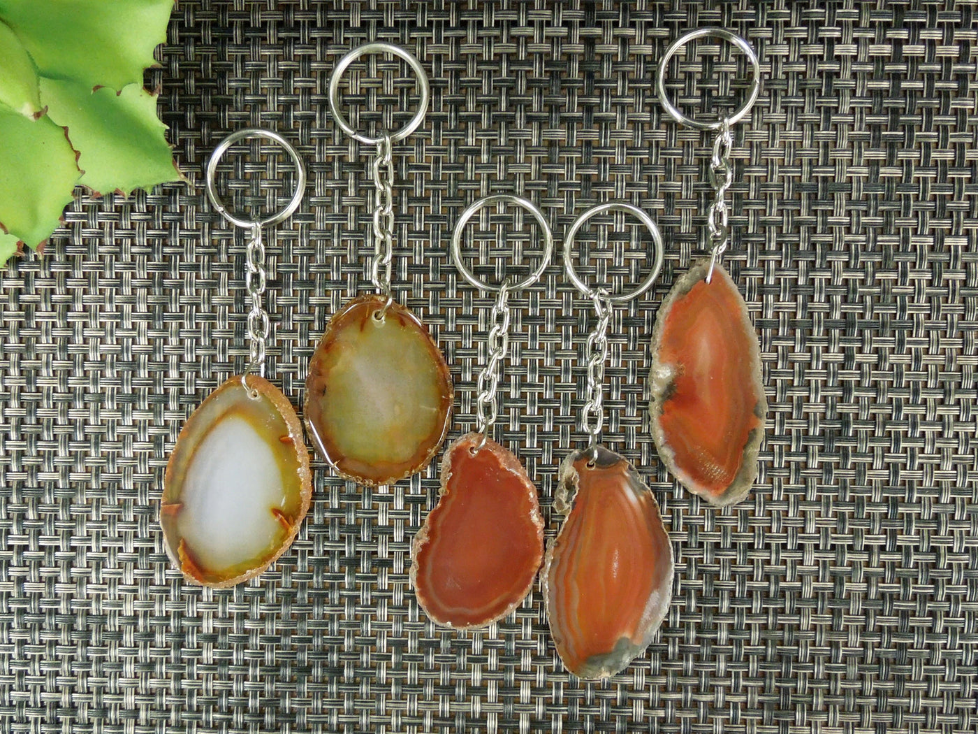 Multiple red agate keychains on a dark colored background displaying color, size, pattern and shape variation.