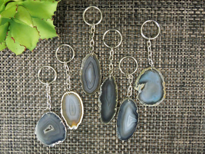 Multiple agate keychains on a dark colored background displaying color, size, pattern and shape variation.