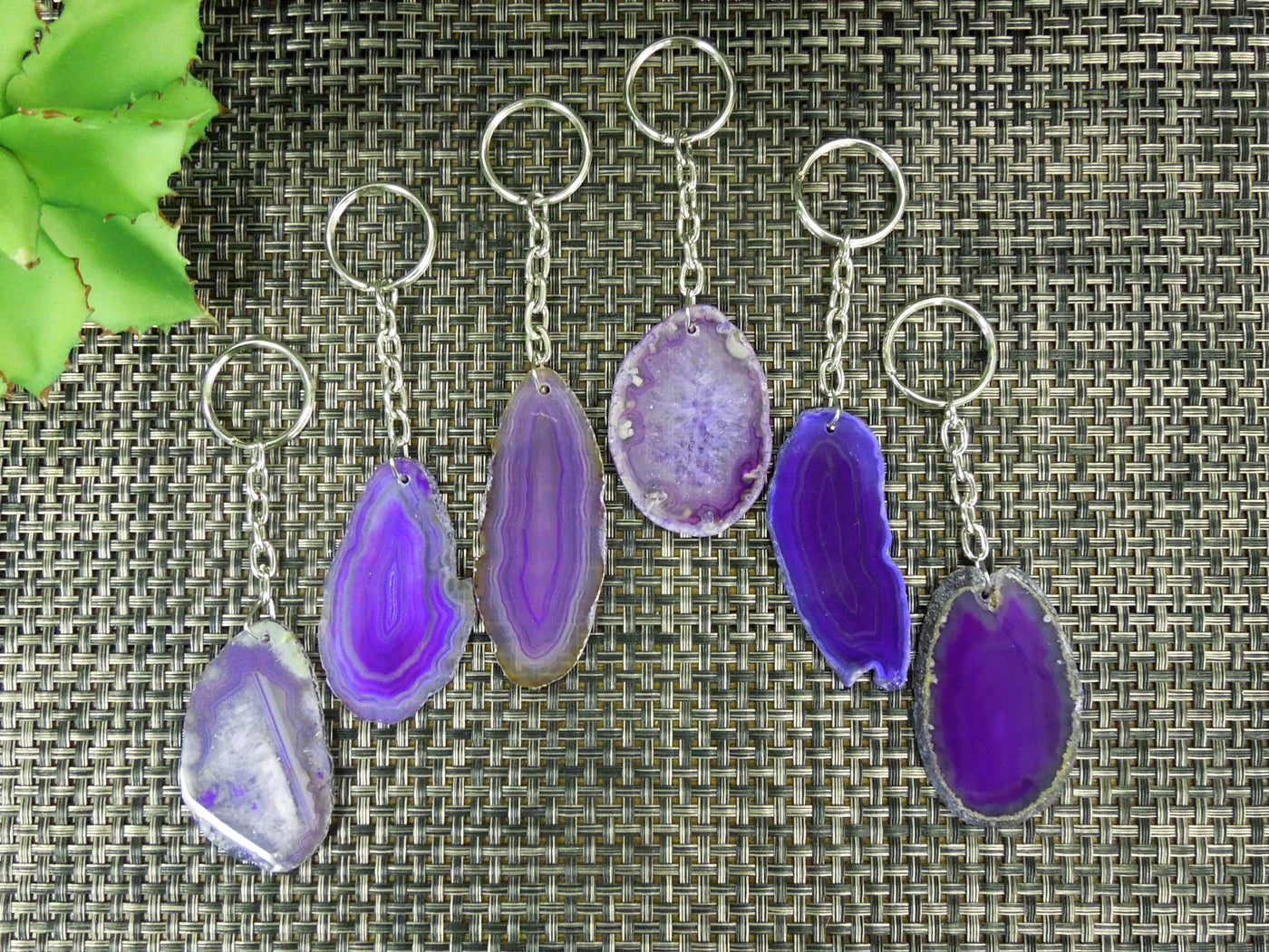 Multiple purple agate keychains on a dark colored background displaying color, size, pattern and shape variation.