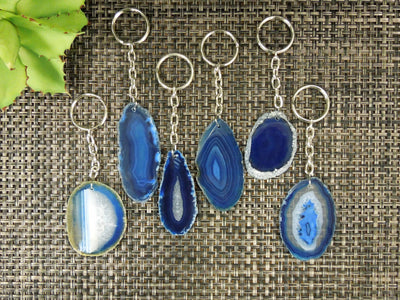 Multiple blue agate keychains on a dark colored background displaying color, size, pattern and shape variation.