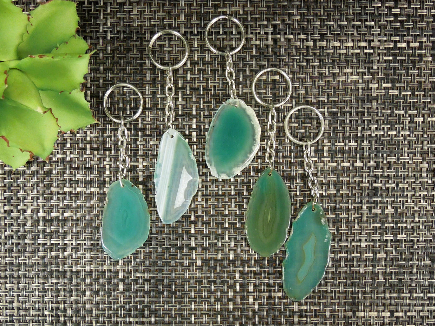 Multiple green agate keychains on a dark colored background displaying color, size, pattern and shape variation.