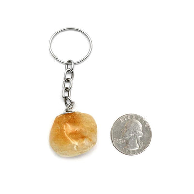 golden amethyst tumbled keychain on white background next to a quarter to show size reference