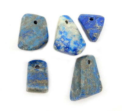 multiple Tumbled lapis lazuli beads displayed on white background to show various shapes sizes natural formations and hues of blues gray gold