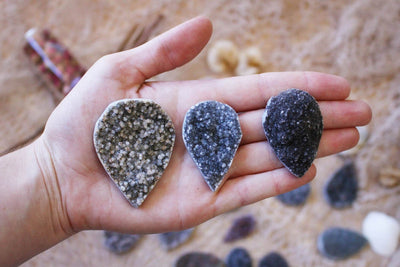 hand holding up 3 large teardrop druzy cabochons with decorations blurred in the background