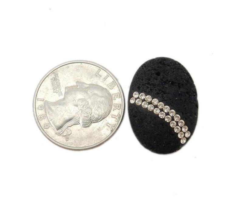 Oval lava stone with two rows of white rhinestones curved across the bottom. Shown next to a quarter showing it is around the same size.