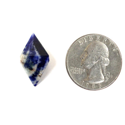 one sodalite diamond shaped point on white background with quarter for size reference