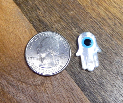 A Mother Of Pearl Hamsa Hand With Eye Accent next to a quarter for size reference 