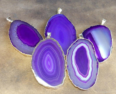 Picture of our purple agate slice pendants being displayed on a dark brown background.