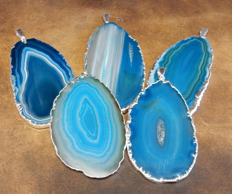Picture of our teal agate slice pendants being displayed on a dark brown background.