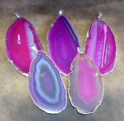 Picture of our pink agate slice pendants being displayed on a dark brown background.