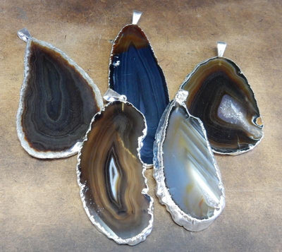 Picture of our black agate slice pendants being displayed on a dark brown background.