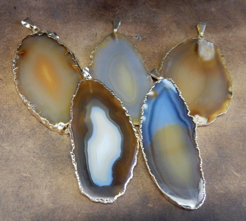 Picture of our natural agate slice pendants being displayed on a dark brown background.