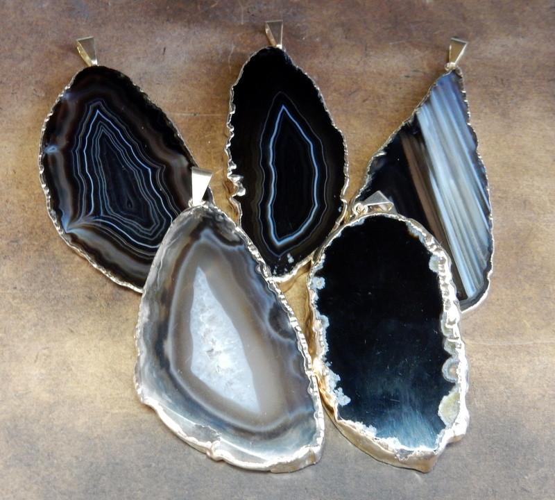 Picture of our Black agate slice pendants being displayed on a dark brown background.