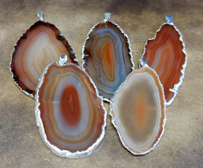 Picture of our Orange/ red agate slice pendants being displayed on a dark brown background.