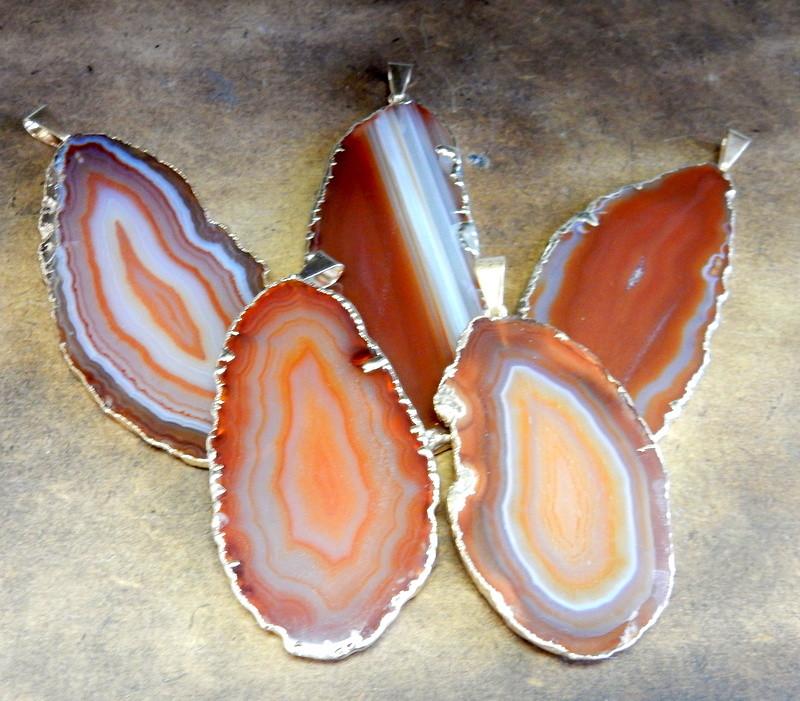 Picture of our Orange/ red agate slice pendants being displayed on a dark brown background. 