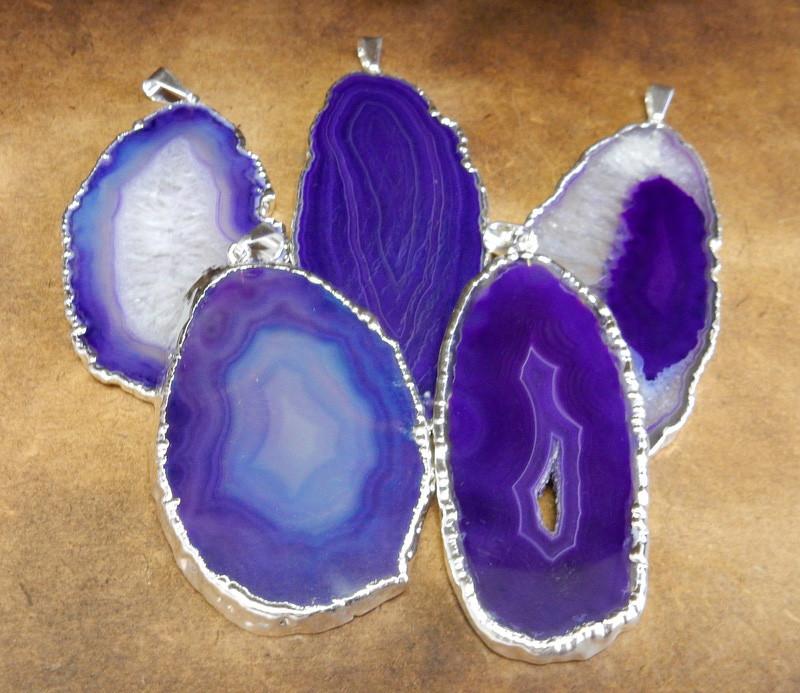 Picture of our purple agate slice pendants being displayed on a dark brown background.